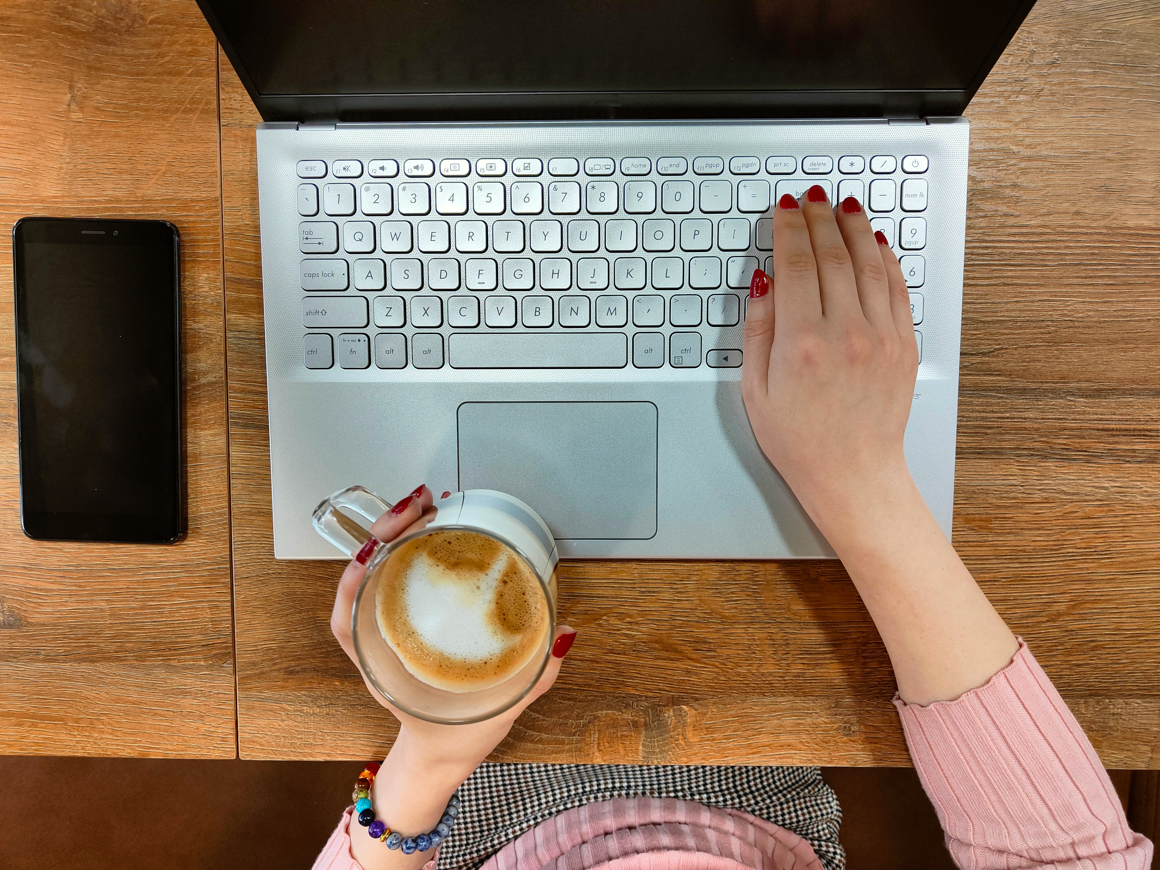 An overhead image of a woman drinking a latte and working on her computer.